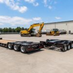 Lowboy and RGN trailers side by side in an industrial yard with heavy construction equipment