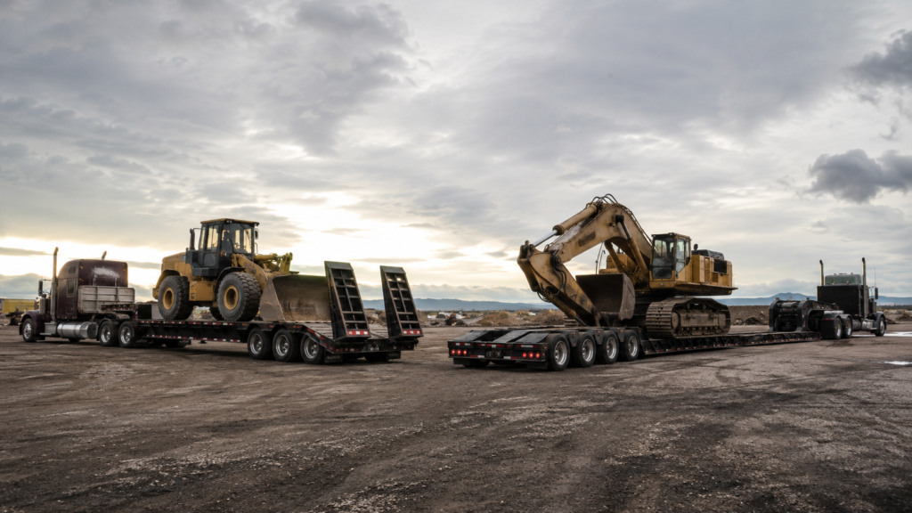 Step deck trailer and RGN trailer carrying heavy construction equipment side by side for comparison.