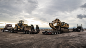 Step deck trailer and RGN trailer carrying heavy construction equipment side by side for comparison.
