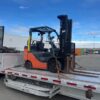 Heavy-duty loading ramps stored beneath the 2023 Extreme step deck trailer carrying a secured forklift