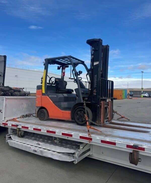 Heavy-duty loading ramps stored beneath the 2023 Extreme step deck trailer carrying a secured forklift