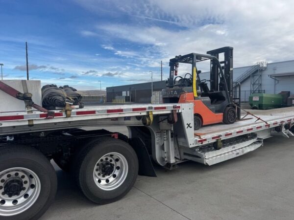 view.jpg Side view of a 2023 Extreme step deck trailer carrying a forklift, with loading ramps stored beneath the lower deck