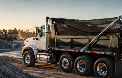 Dump truck with a tarp system covering the truck bed at a U.S. aggregate site for safer, more efficient load transport.