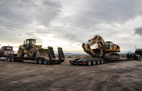 Step deck trailer and RGN trailer carrying heavy construction equipment side by side for comparison.